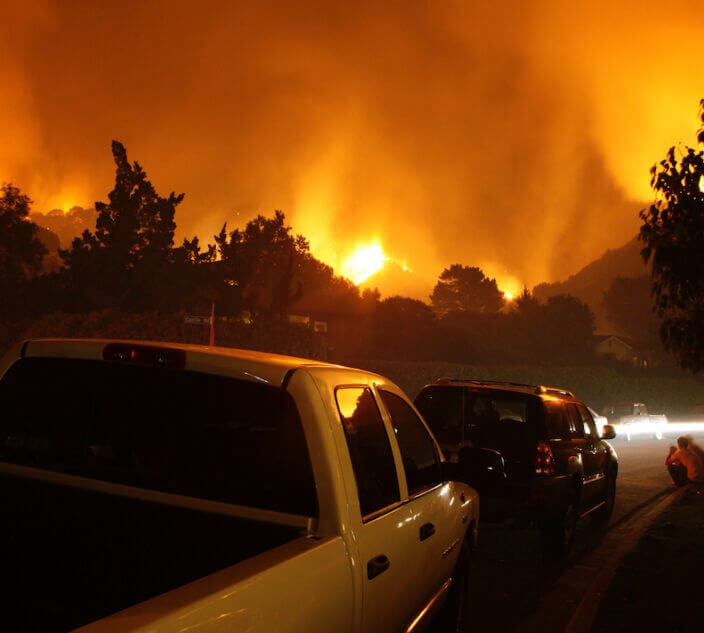 Residents of a neighborhood sit by and watch a fire threaten their homes.